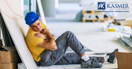 worker sitting on the ground holding their shoulder with an injury